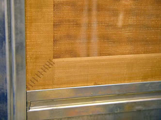 A piece of brass woven wire mesh is installed onto the aluminum window frame.