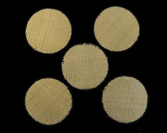 Five pieces of brass tobacco pipe filter discs on the black background.